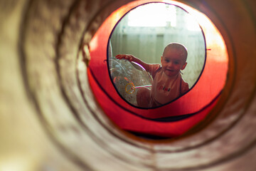 A cute little girl leaning on the transparent air balloon and looking on camera through a colourful tunnel.