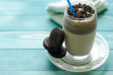 Milkshake (chocolate smoothie)  in a glass on colorful turquoise blue painted wooden boards. Selective focus on cookies in glass