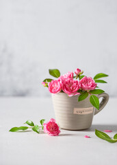 Delicate pink mini roses in a small cup in beige color. Still life with summer flowers. Copy space.