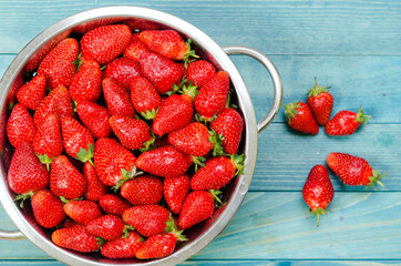 Fresh strawberries in retro colander on rustic aqua blue wooden boards.