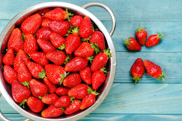 Fresh strawberries in retro colander on rustic aqua blue wooden boards.
