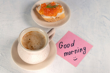 a cup of coffee with a sandwich with red caviar and next to a note with the words good morning. top view.