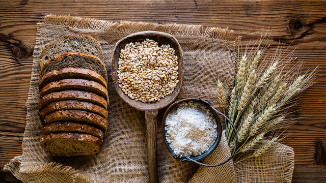 Sliced wholemeal bread with cereals and various seeds, wholemeal flour, barley grains and ears of wheat on jute cloth. view from top.