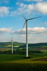 Wind power plant consisting of two wind turbines in an agricultural landscape, with blue sky and...