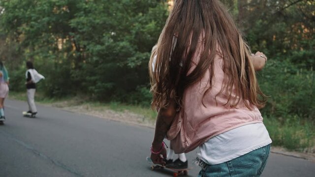 Teenagers skate along the forest road. A group of young people, the millennial generation, ride skateboards, have fun. Youth subculture, sports and hobbies