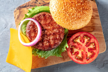 Burger ingredients on a wooden board close-up. Juicy bbq grilled beef patty with onion, tomato, cheese, lettuce and sesame bread buns, top shot