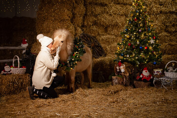 Christmas decorations on the stables. A pony with a wreath around his neck. Christmas tree with...
