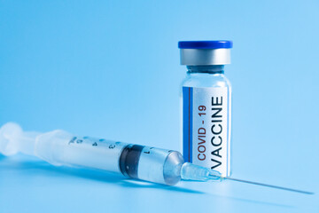 Closeup single vial of Covid 19 vaccine with syringe on cyan background.