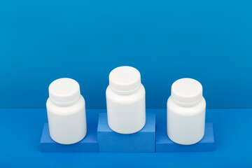 Creative composition with three white medication bottles on winner pedestal against blue background. High angle view, copy space. Concept of medical treatment and pharmaceutical industry