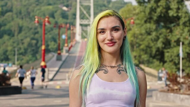 Teenager with multi-colored yellow blue hair, tattoos, piercings and a tunnel in the earlobe. Youth subculture concept. Close outside portrait of a young girl with a bright appearance