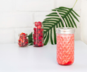 still life with a bottle of berry smoothie, berries in jars, and a branch of palm