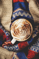 Pumpkin latte with whipped cream and syrup on folk knitted sweater. Top view, flat lay.
