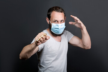 Metal brass knuckles in the hand of a bearded man in a surgical mask. forbidden weapons in a fight,...
