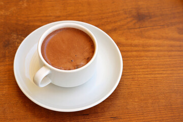 Fototapeta premium Cup of hot chocolate in a white saucer on wooden table, cocoa drink