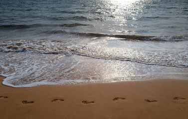 Footprints at golden sand, footsteps. Beach background. Calm beautiful ocean wave on sandy beach. Sea view from tropical sea beach.