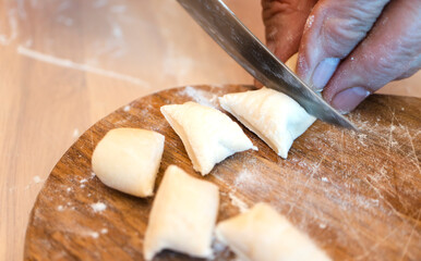 Fototapeta na wymiar Female hands cut pieces of dough for dumplings with a knife on a wooden board. High quality photo