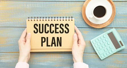 SUCCESS PLAN text written in a notebook lying on a wooden work table
