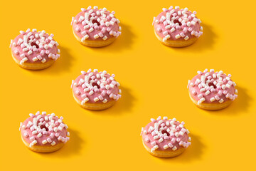 Many pink donuts with marshmallow topping on yellow background. pattern image