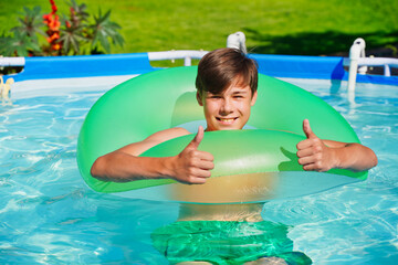 Young man plays active games in the pool, thumbs up, recommend summer fun and entertainment. Teenager spends time outdoors