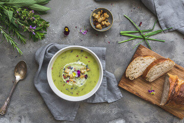 Creamy herbes soup with potatoes, herbes and sorrel, with edible blooms and croutons as topping. Gray concrete background. Top view.