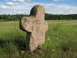 An old pagan cemetery in Belarus. Stone pink cross made of granite. humanlike