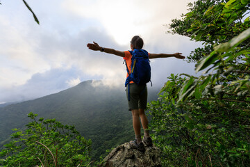 Cheering young woman hiker open arms on mountain peak