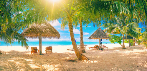 Beautiful sandy beach on the Maldives island in shade of green palm trees and thatched umbrellas with sun loungers.
