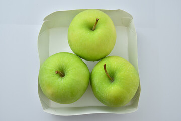 Three green apples in a cardboard box