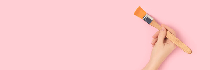 Female hand hold paintbrush on a pink pastel background. Repair concept with copyspace.