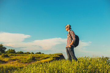Smiling young man with a backpack stands on the trail looking at the panorama while walking alone, Tourist with a backpack looking
