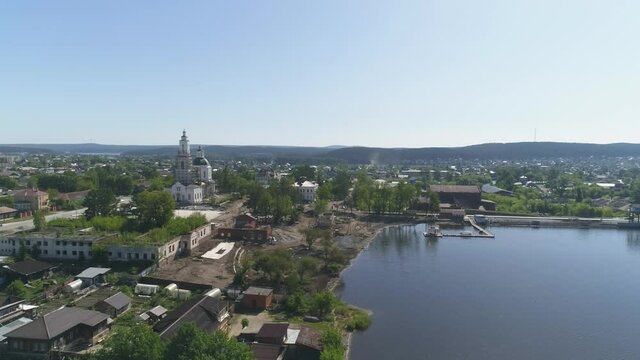 Aerial view of Construction of a embankment in the provincial town. Reconstruction of the old church and old houses. Next to the pond is an old factory. Trees and building materials on the shore. Summ