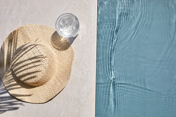 Summer vacation. Hat on the travertine stone by the beautiful swimming pool. Blue sea surface with...