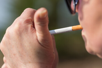 Middle age woman catch fire cigarette outdoors with sun on her face.Closeup woman with cigarette in her mouth copy space
