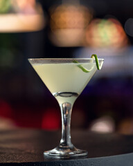 Alcoholic drink. Martini glass with lime decor on dark background, abstract blurred image. Copy space.