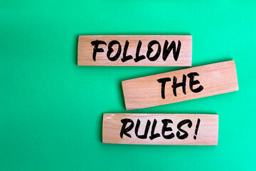 Follow The Rules! words made on wooden building blocks green background.