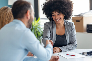 Attractive real-estate agent shaking hands with young couple after signing agreement contract in...