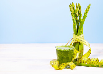 Bunch of fresh asparagus and green smoothie on blue background with Measuring tape. Ketogenic diet food with vitamins and cellulose. Copy space. Clean eating concept.