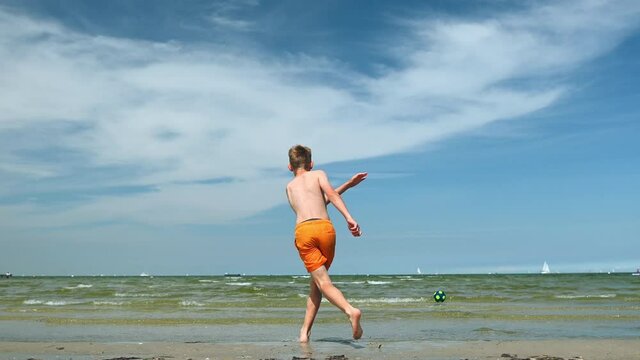 4K video of happy teen boy playing with ball on beach at sunny day while summer holidays