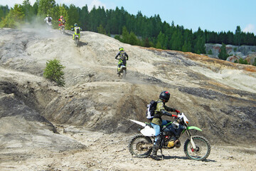 Four motorcyclists climb up a clay slope. The fifth biker stayed downstairs and watched the departing motorcyclists. All bikers are dressed in bright clothes and helmets.