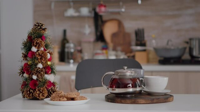 Xmas decorated kitchen with nobody in it during winter season waiting for guest. On table standing baked homemade traditional delicious cookies and cup of coffee with christmas tree beside