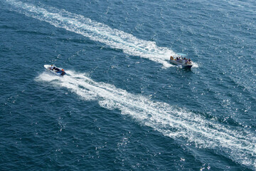 Two white and blue boats sail in different directions on the blue sea. White, foamy footprints follow the boats. The direction of movement of vessels is opposite. Boats is carrying a group of turists.