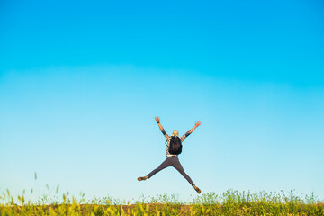 Rear view of man jumping up with outstretched arms, happy man with arms up against blue sky background, outdoors