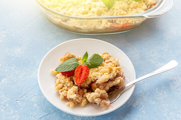 Home сooking. Rhubarb or Strawberry crumble, gluten free crisp in baking dish. Summer dessert on plate on blue background.