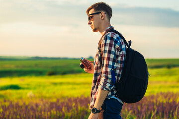 Young male tourist, in sunglasses, with a camera, in nature, spending time in a hike, on the field