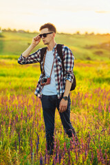 Young male tourist, in sunglasses, with a camera, in nature, spending time in a hike, on the field