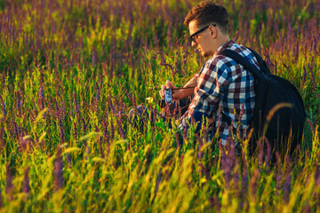 Naklejka na ściany i meble Young male tourist, in sunglasses, with a camera, in nature, spending time in a hike, on the field
