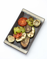 Grilled vegetables on platter. Clay plate with fried zucchini, eggplant, bell pepper, tomato and onion isolated on white background. Top view.