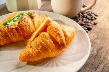 croissant in white plate, coffee beans, and coffee kettle on old wooden table.soft focus.
