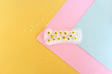 A sanitary pad with chamomile flowers lies on a colorful background.