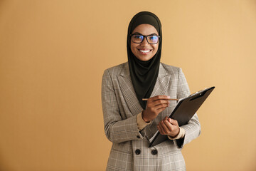 Black muslim woman in eyeglasses writing down notes on clipboard